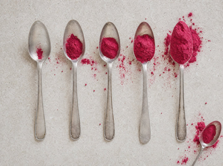 Fünf Esslöffel nebeneinander, von fast leer bis gehäuft voll mit rosa Fruchtpulver