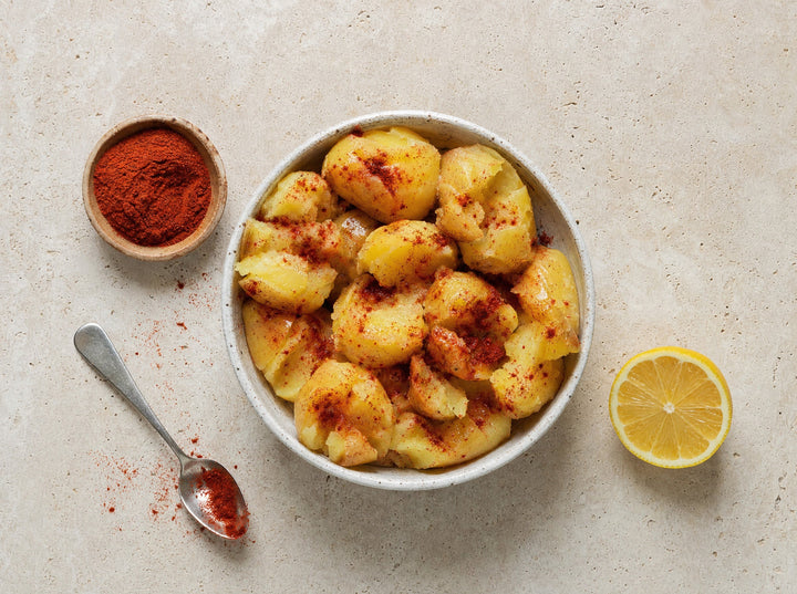 Eine Schale gekochte Kartoffeln mit Tomatenpulver, daneben eine halbe Zitrone