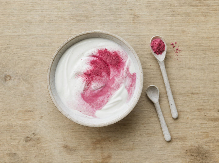 Eine kleine Kinderschale Naturjoghurt mit eingerührtem rosa Pulver und zwei Löffeln