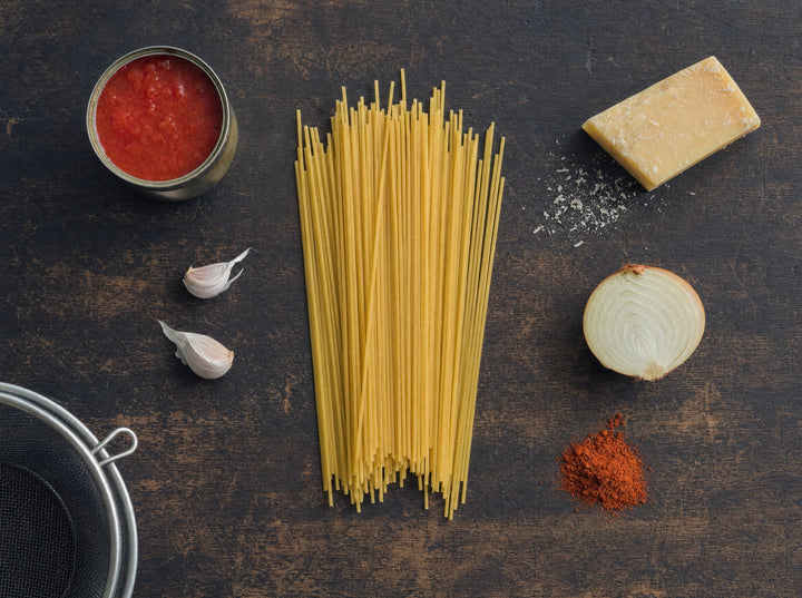 Spaghetti, eine Dose Tomaten, Knoblauch, Hartkäse und eine halbe Zwiebel auf dunklem Holz