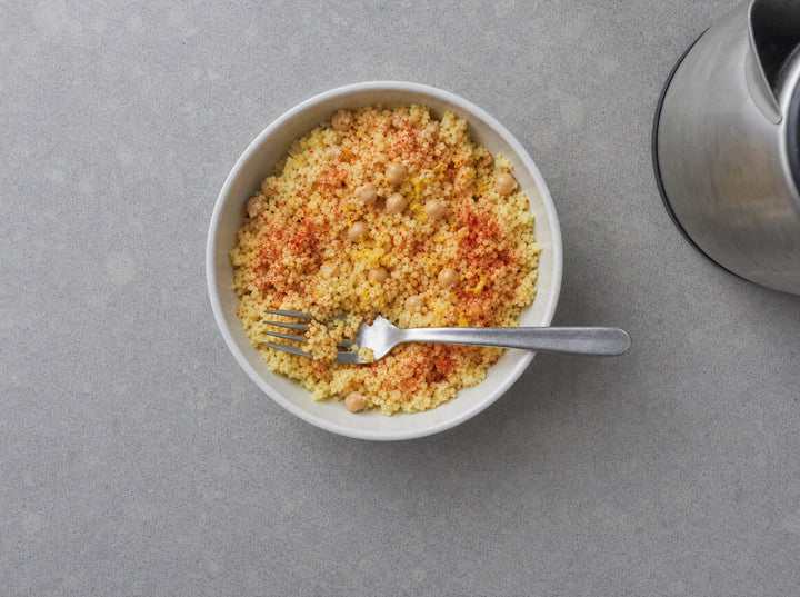 Eine Schüssel Couscous mit Tomatenpulver und Kichererbsen, daneben ein Wasserkocher