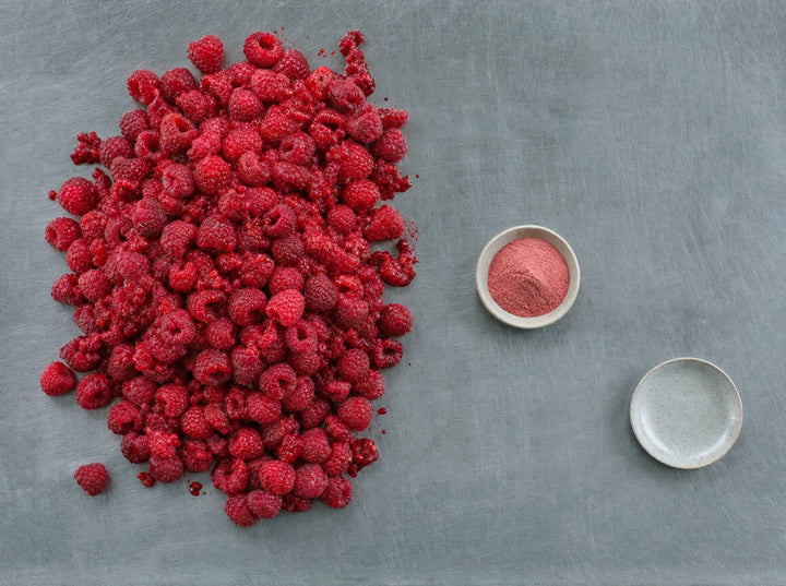 Ein großer Berg frischer Himbeeren neben einer kleinen Schale Fruchtpulver