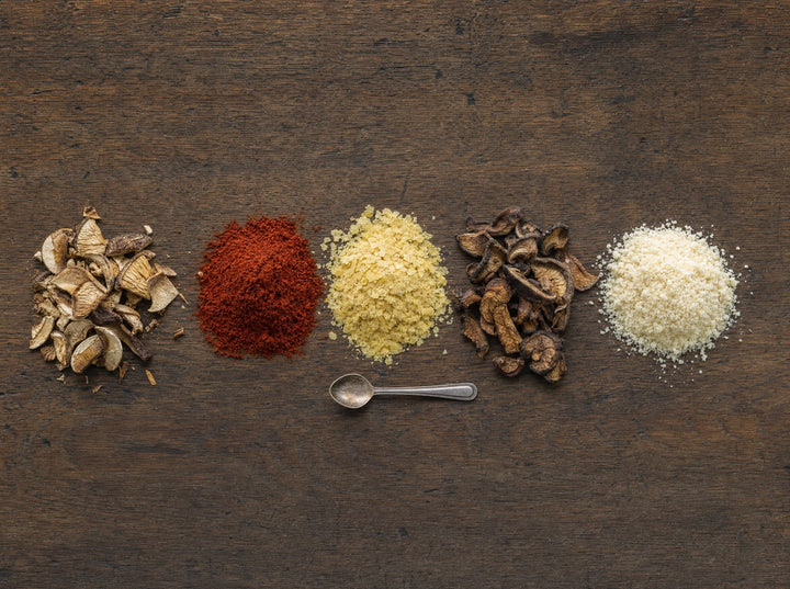 Fünf Häufchen auf dunklem Holz: Steinpilze, Tomatenpulver, Nährhefe, Shiitake, Parmesan