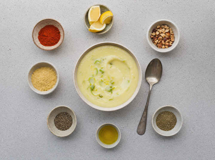 Eine Schüssel helle Suppe, ringsum sieben Schälchen mit verschiedenen Würzzutaten