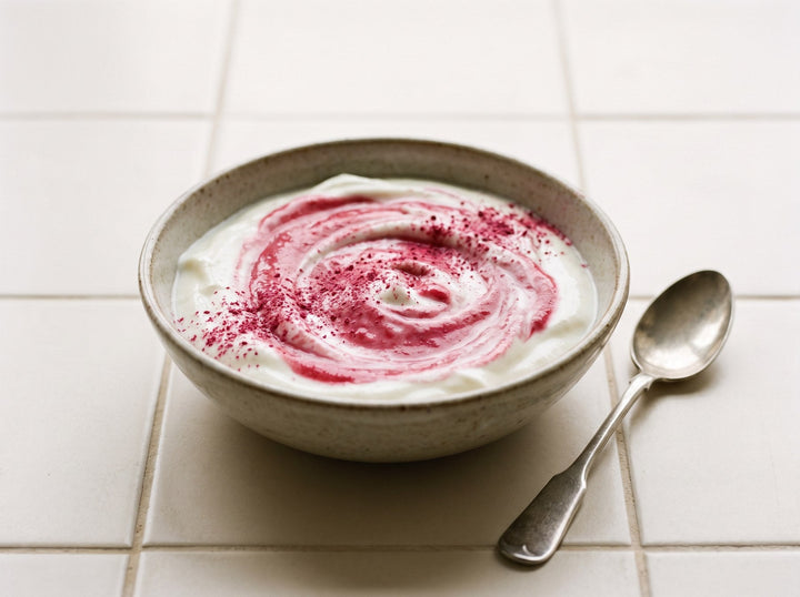 Schüssel mit pink eingerührtem Naturjoghurt und frischen Himbeeren