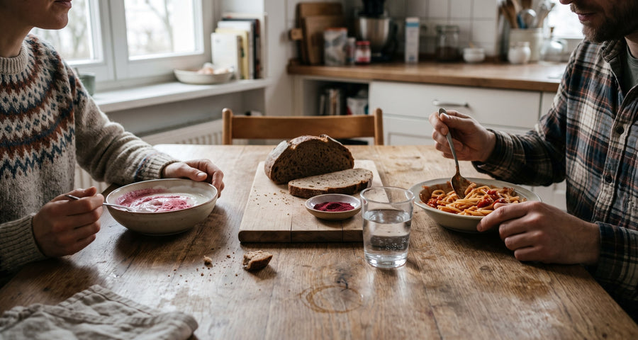 Zwei Erwachsene am Kuechentisch, Joghurt mit Fruchtpulver, Pasta und Brot