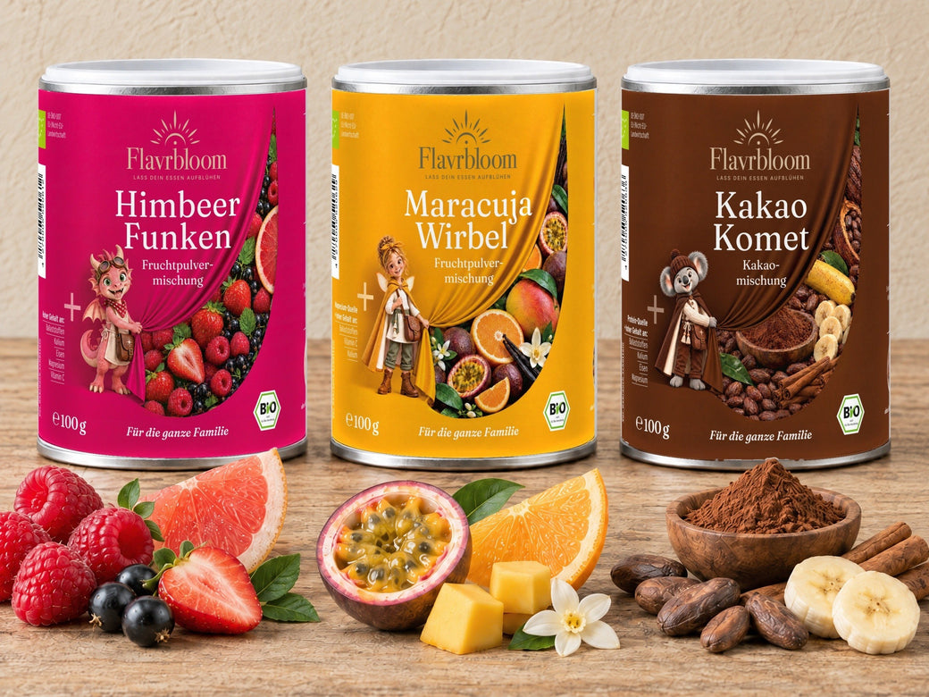 Die süßen Drei: Himbeer Funken, Maracuja Wirbel und Kakao Komet auf Holz, davor Beeren, Maracuja, Mango, Kakaobohnen und Banane
