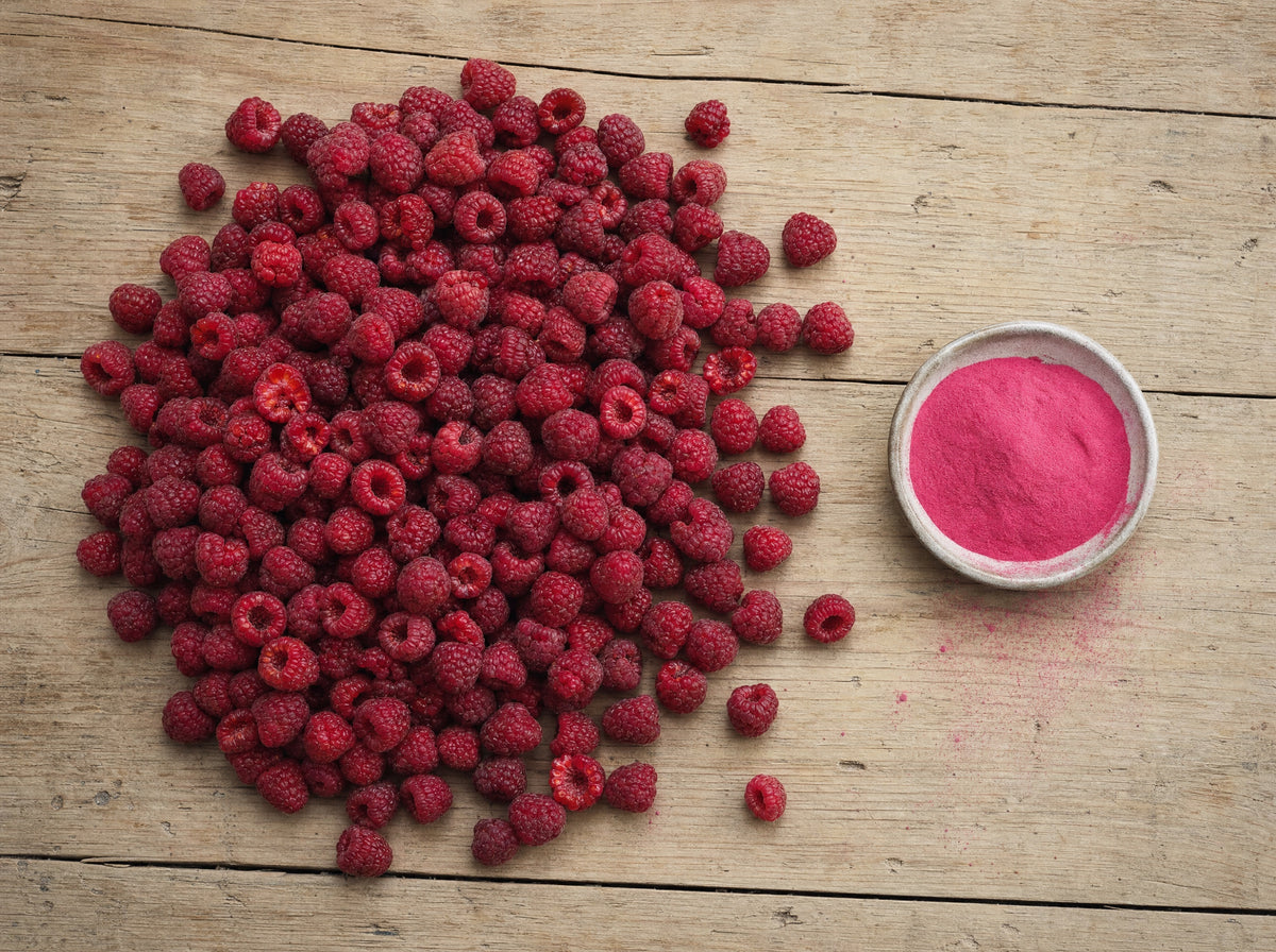 Ein grosser Haufen frischer Himbeeren neben einer kleinen Schale mit pinkem Himbeerpulver